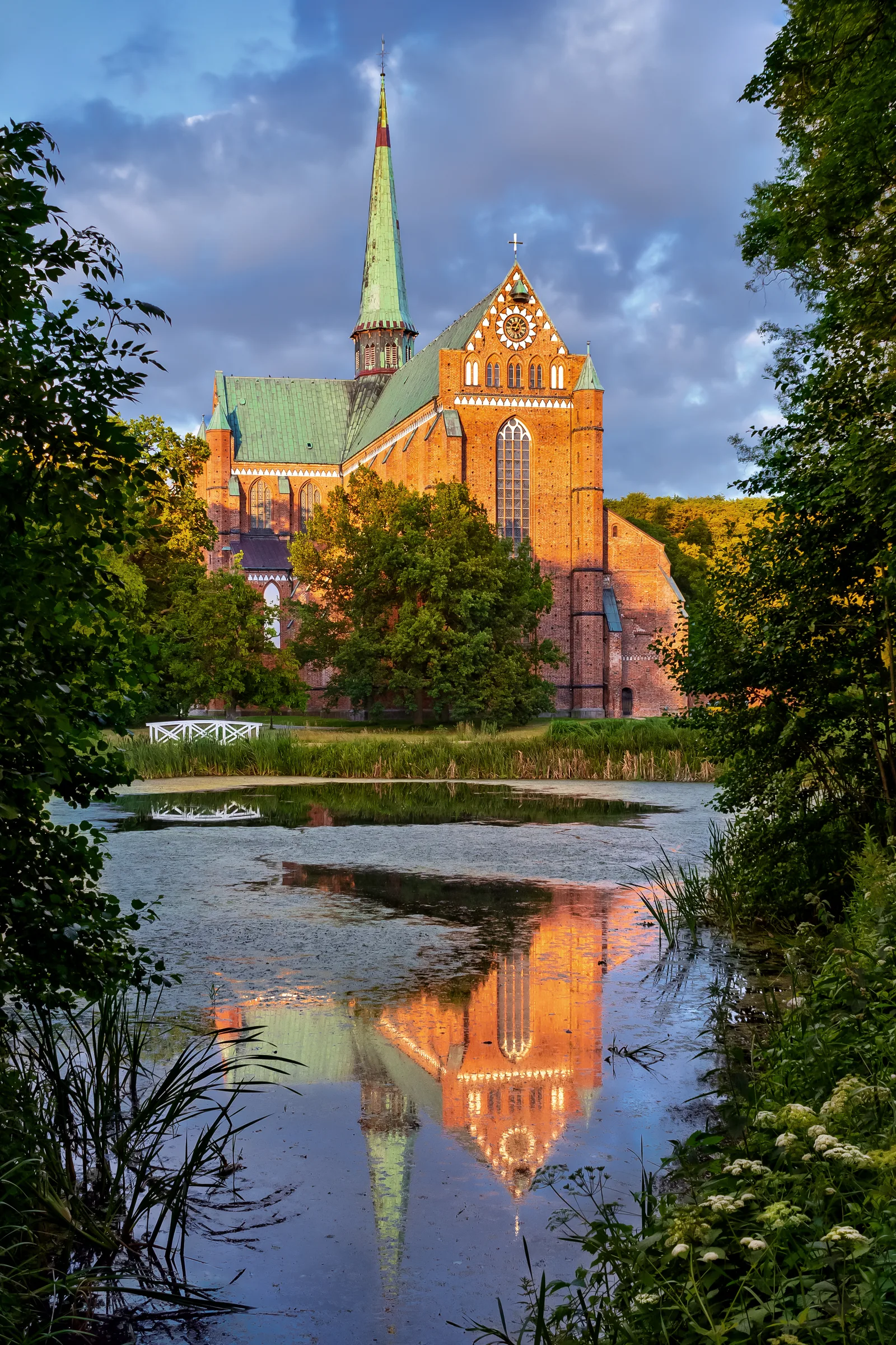 Northwest view of the Doberan Minster during the golden hour , with its reflection in the pond of the Johann Sebastian Bach Park, Bad Doberan , Germany