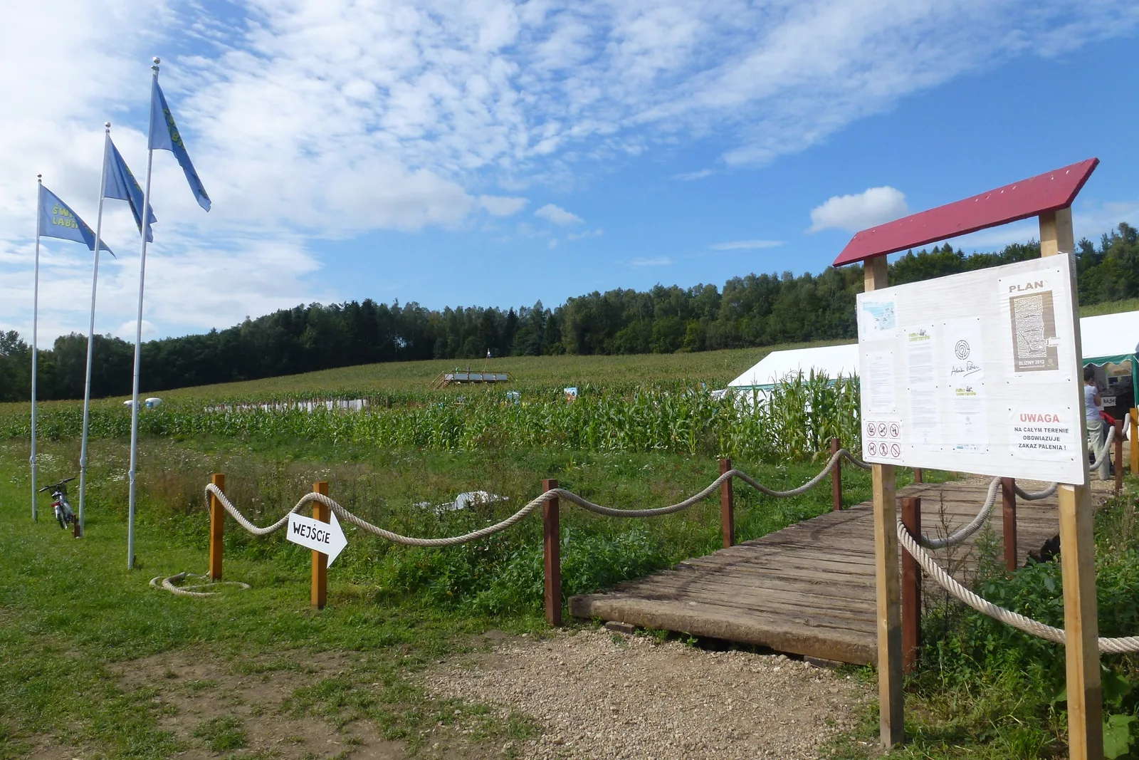 wejście do labiryntu w polu kukurydzy w Blizinach, z flagami, kładką i tablicą z planem