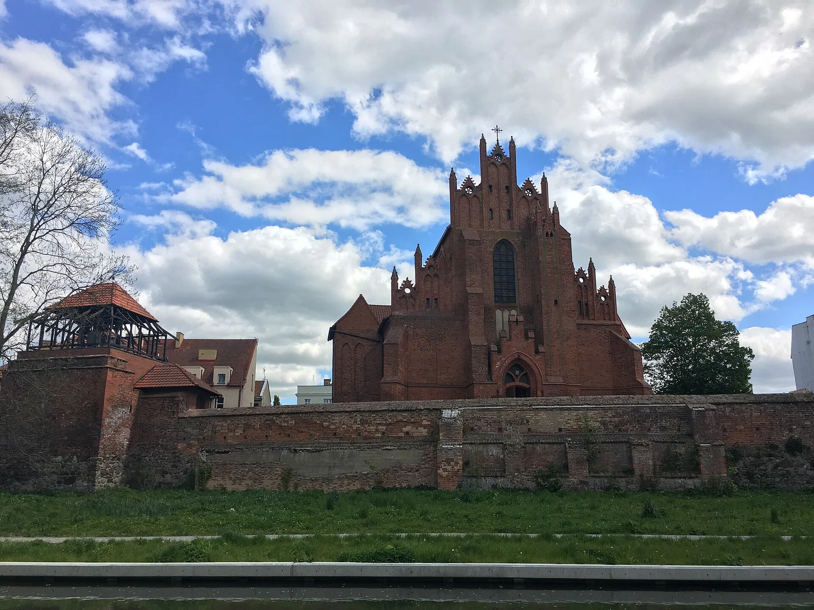 Fara pw. św. Mateusza w Starogardzie Gdańskim, widok na fasadę od strony parku miejskiego, widoczne mury miejskie oraz kostnica z wbudowaną w nią dzwonnicą z 4 dzwonami.